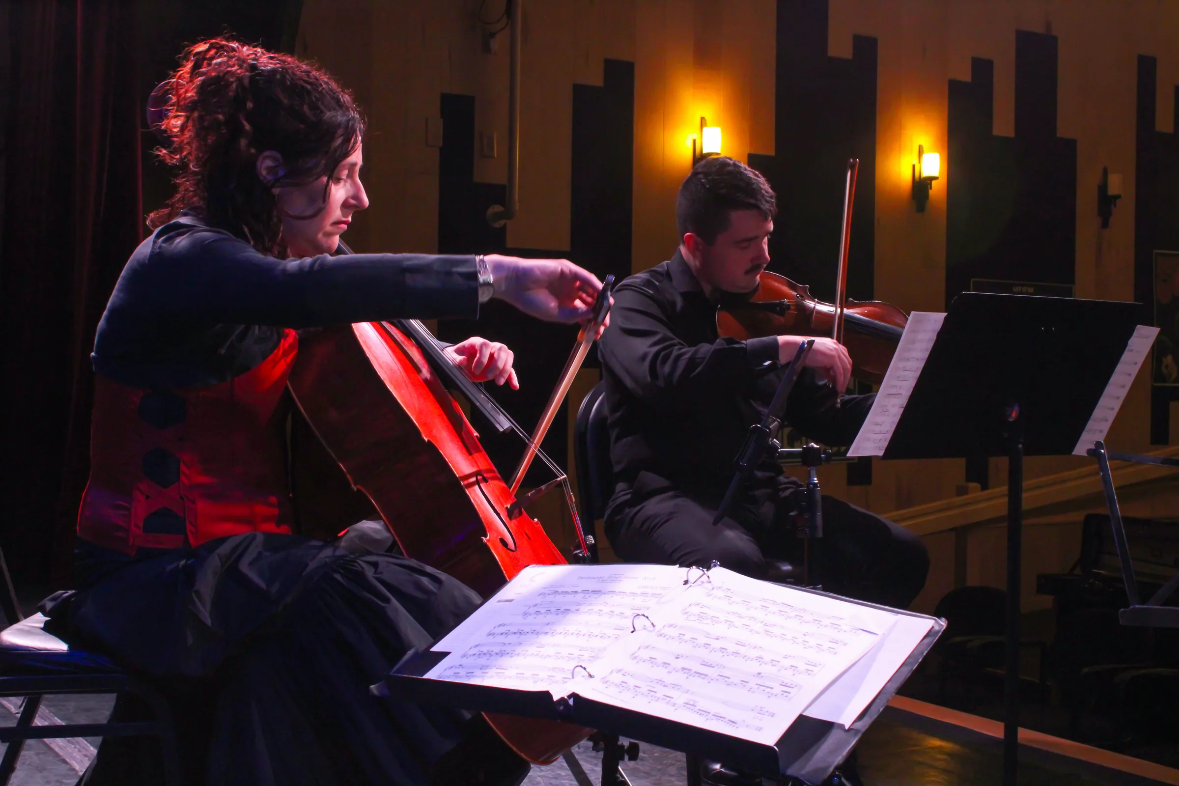 A cellist and violinist performing by lamplight