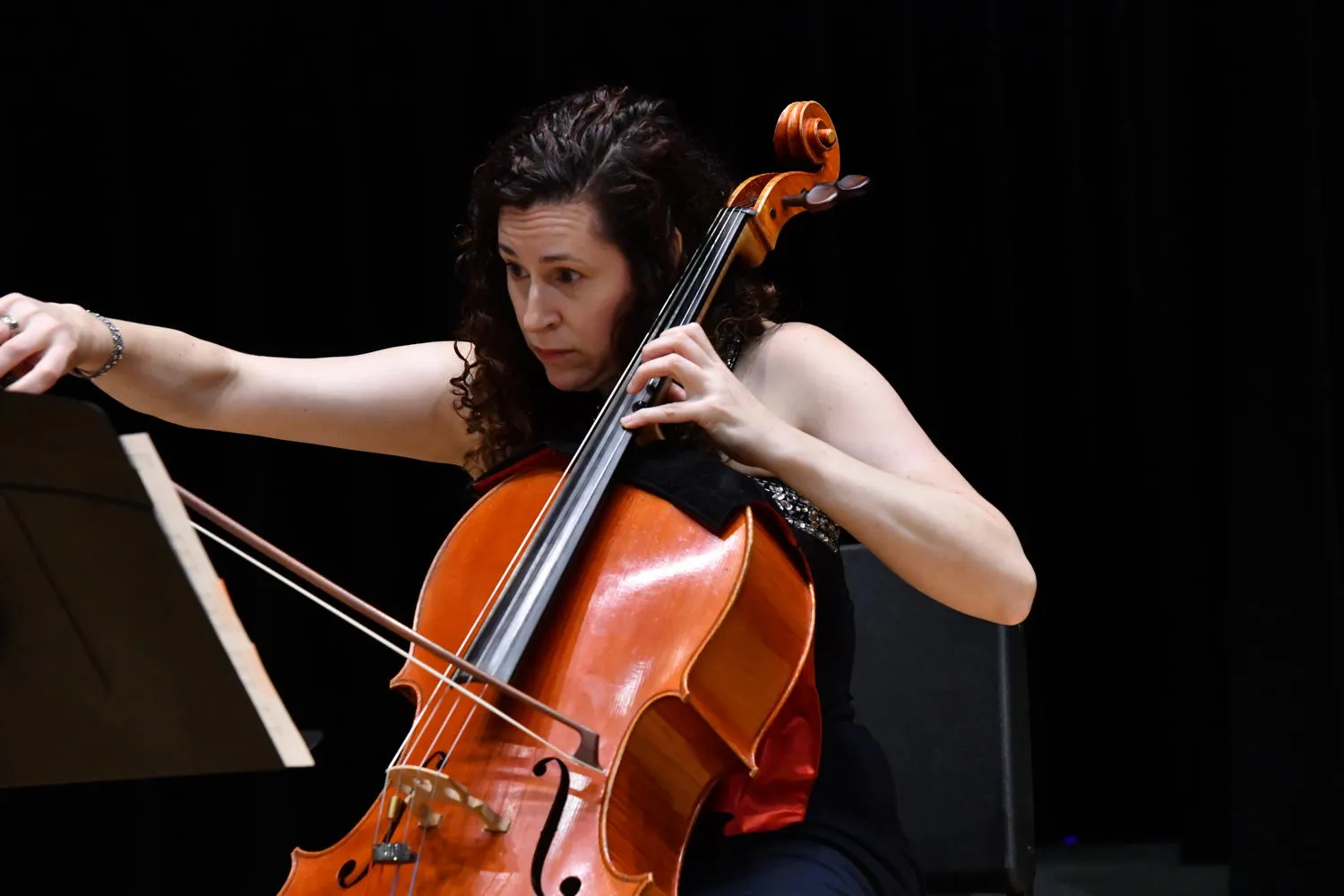 A cellist with curly hair playing against a dark backdrop