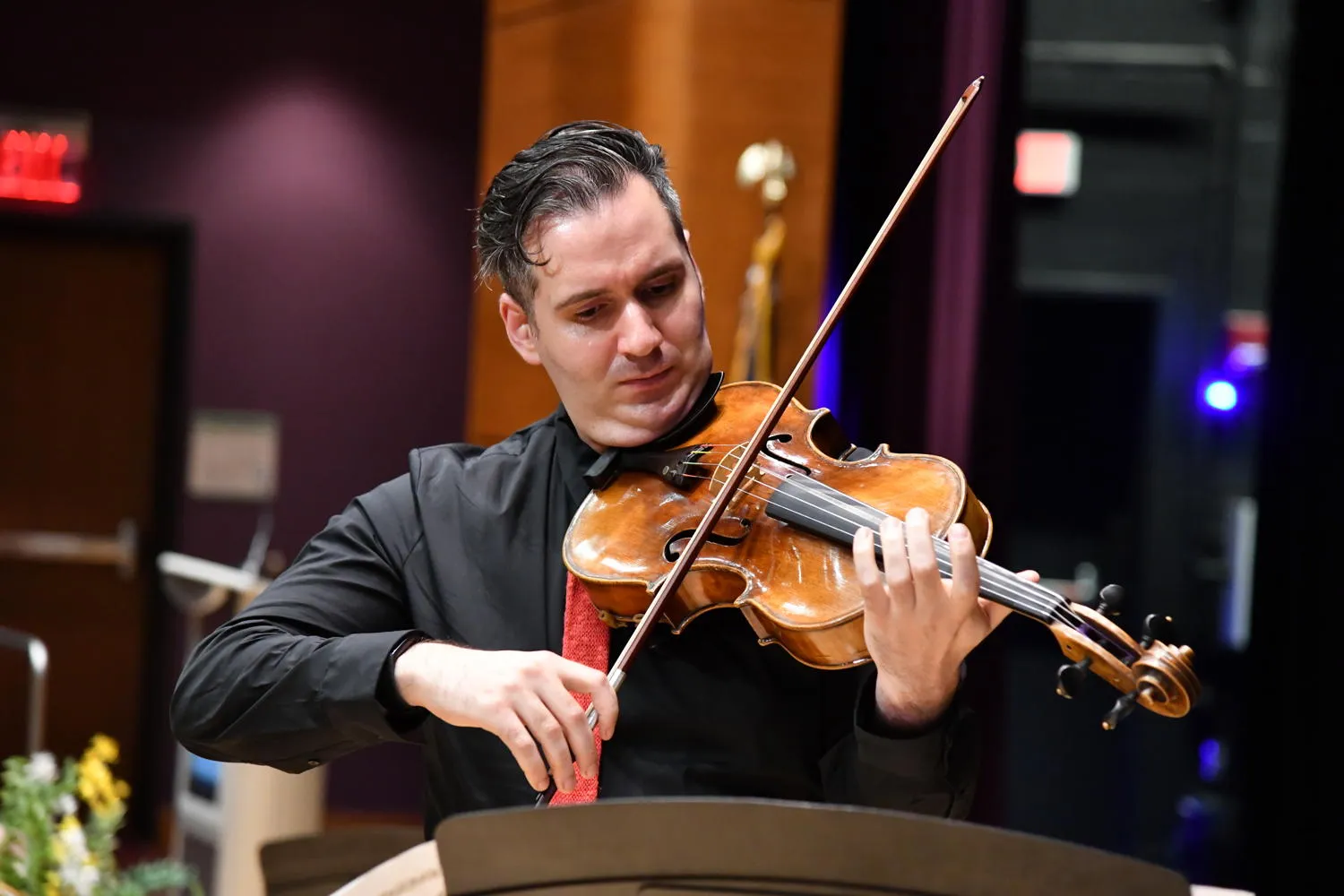 A violinist in a black shirt and red tie playing on stage
