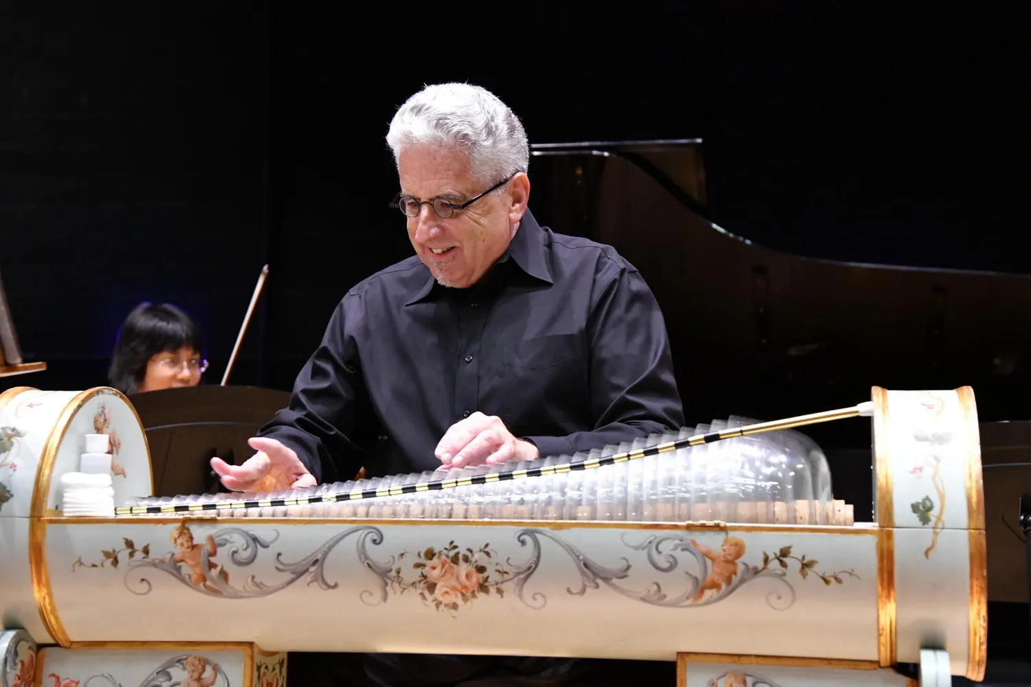 Dennis James smiling while playing the glass armonica, a string player behind