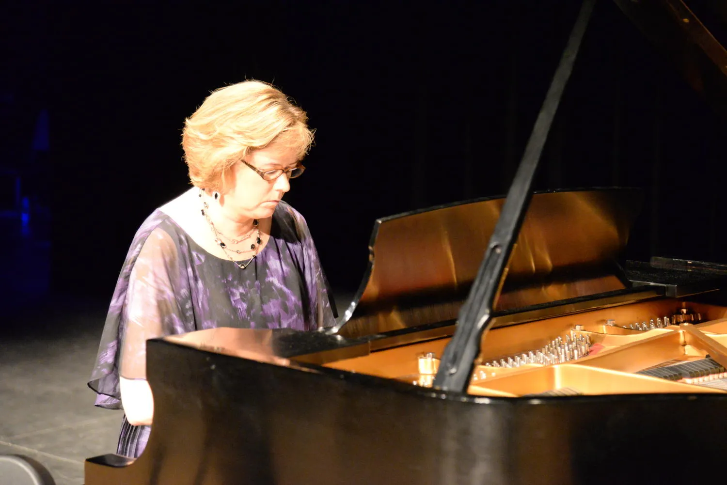 A pianist in a purple top playing a grand piano under warm stage light