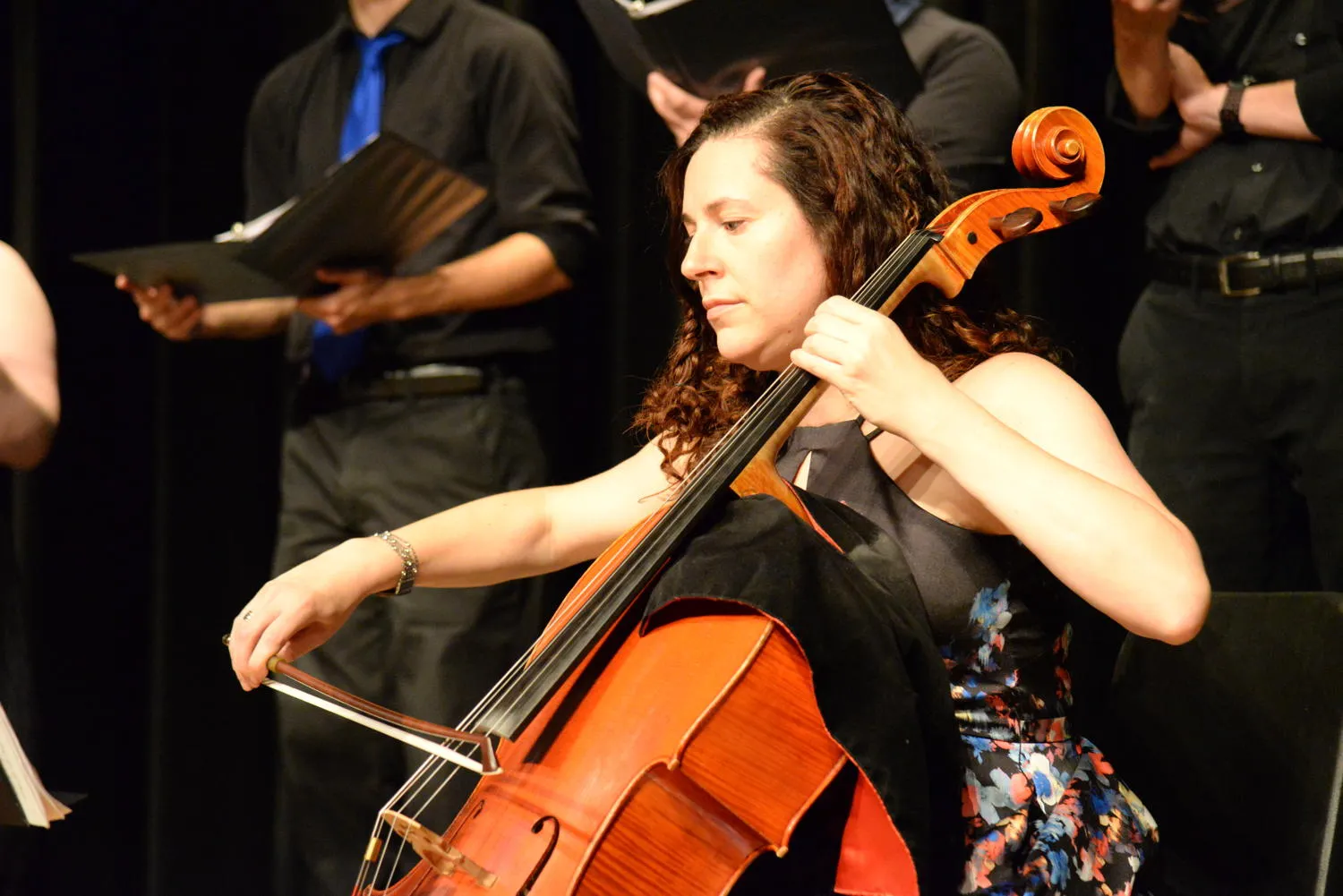 A cellist playing in front of singers holding black folders