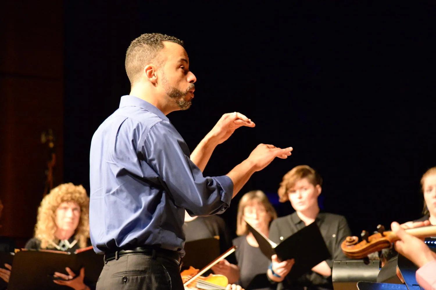 A conductor in a blue shirt leading singers holding black folders