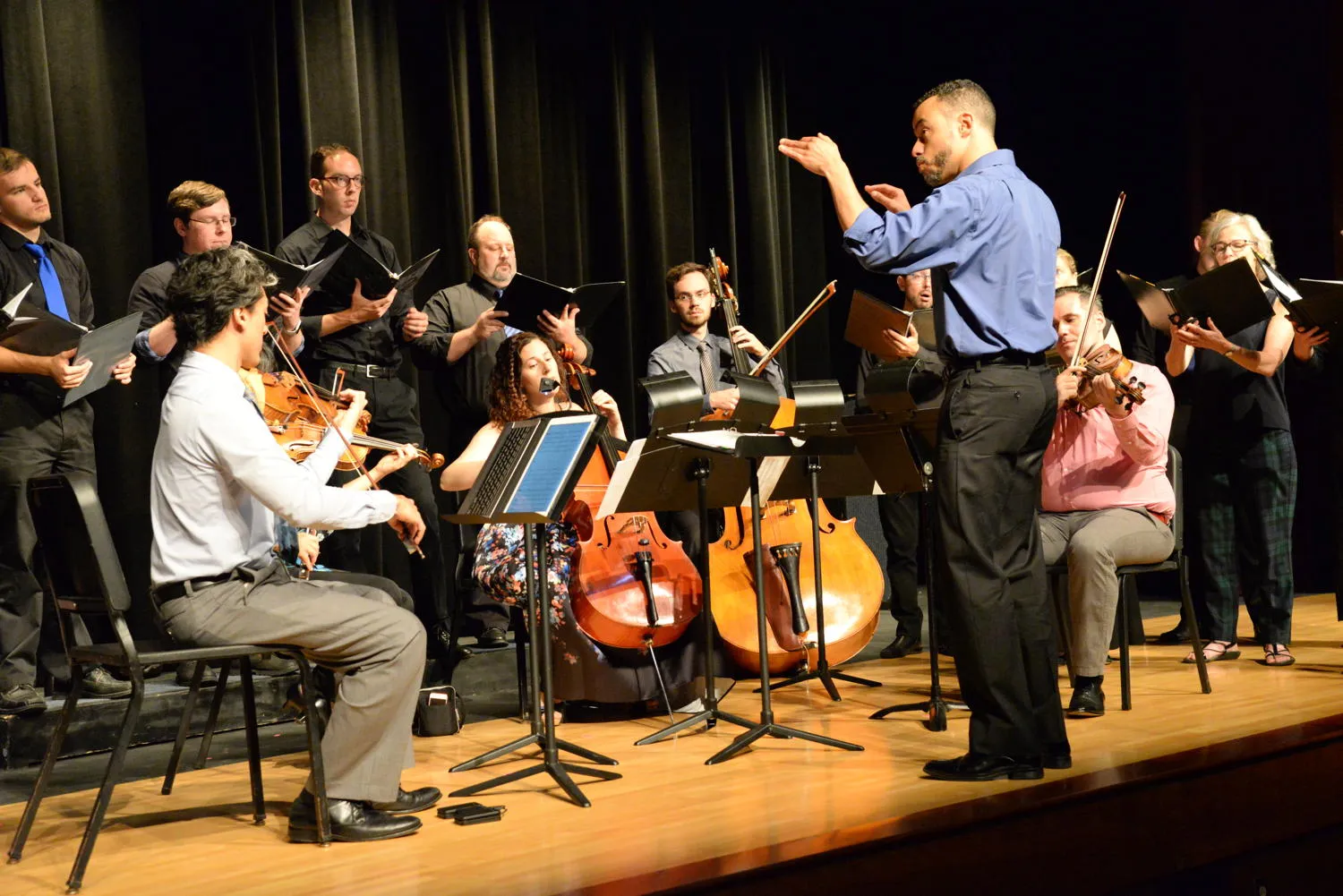 A conductor leading singers and string players on stage