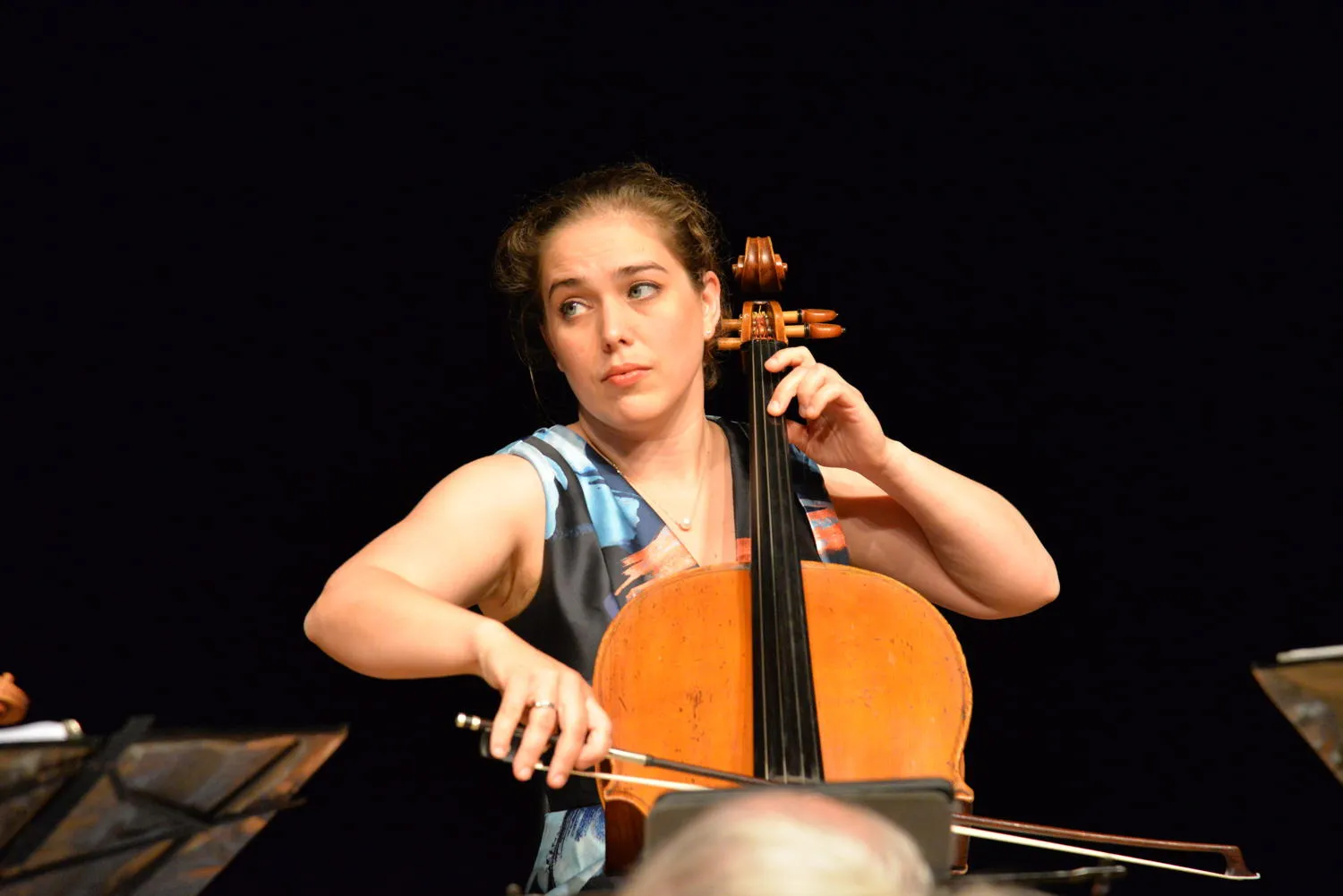 A cellist in a blue patterned dress glancing to the side while playing