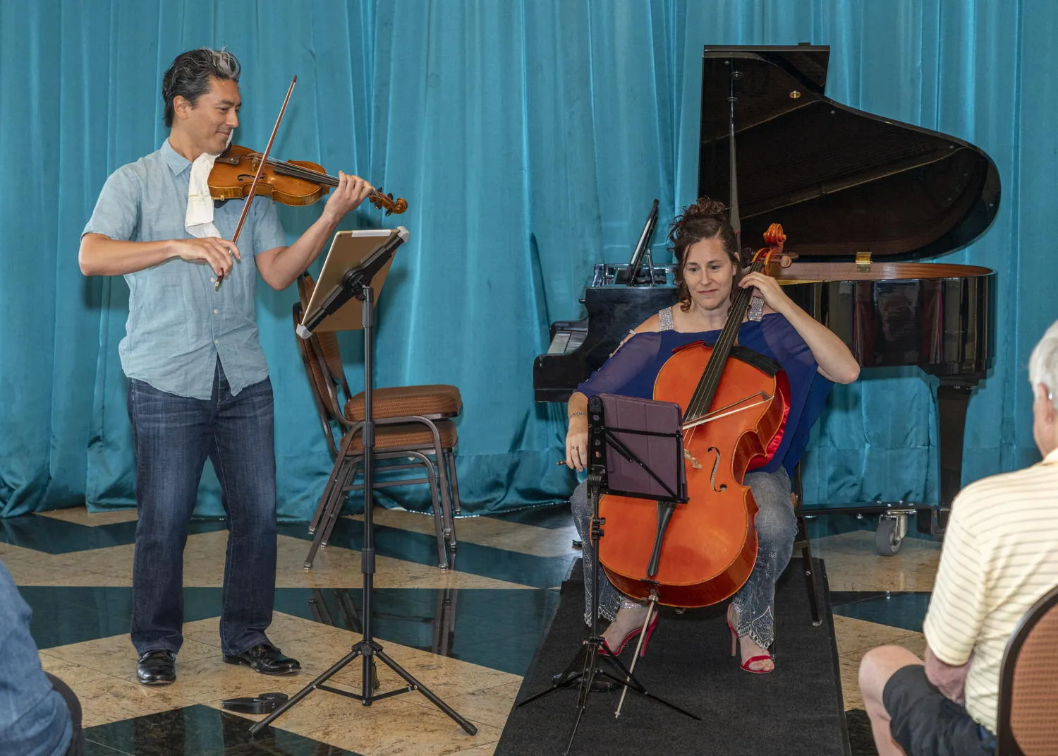 A violinist and a cellist performing before a teal curtain and a grand piano