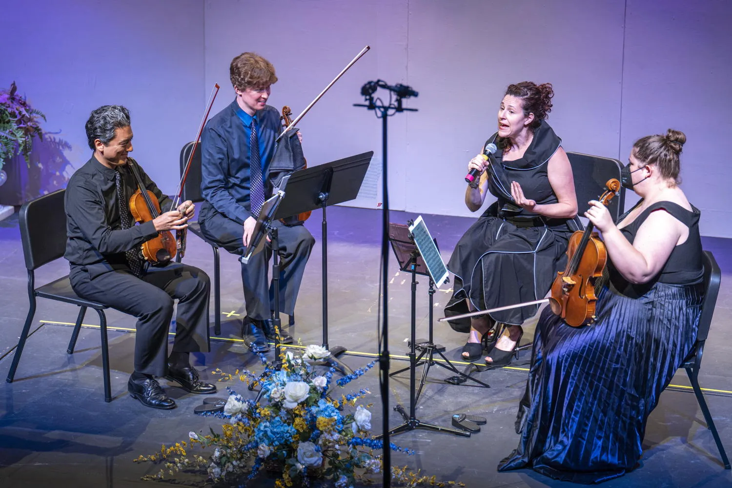 A string quartet on stage as one member speaks into a microphone