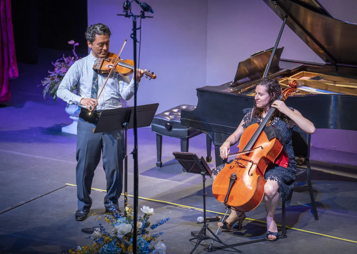 A violinist and a cellist performing beside a grand piano