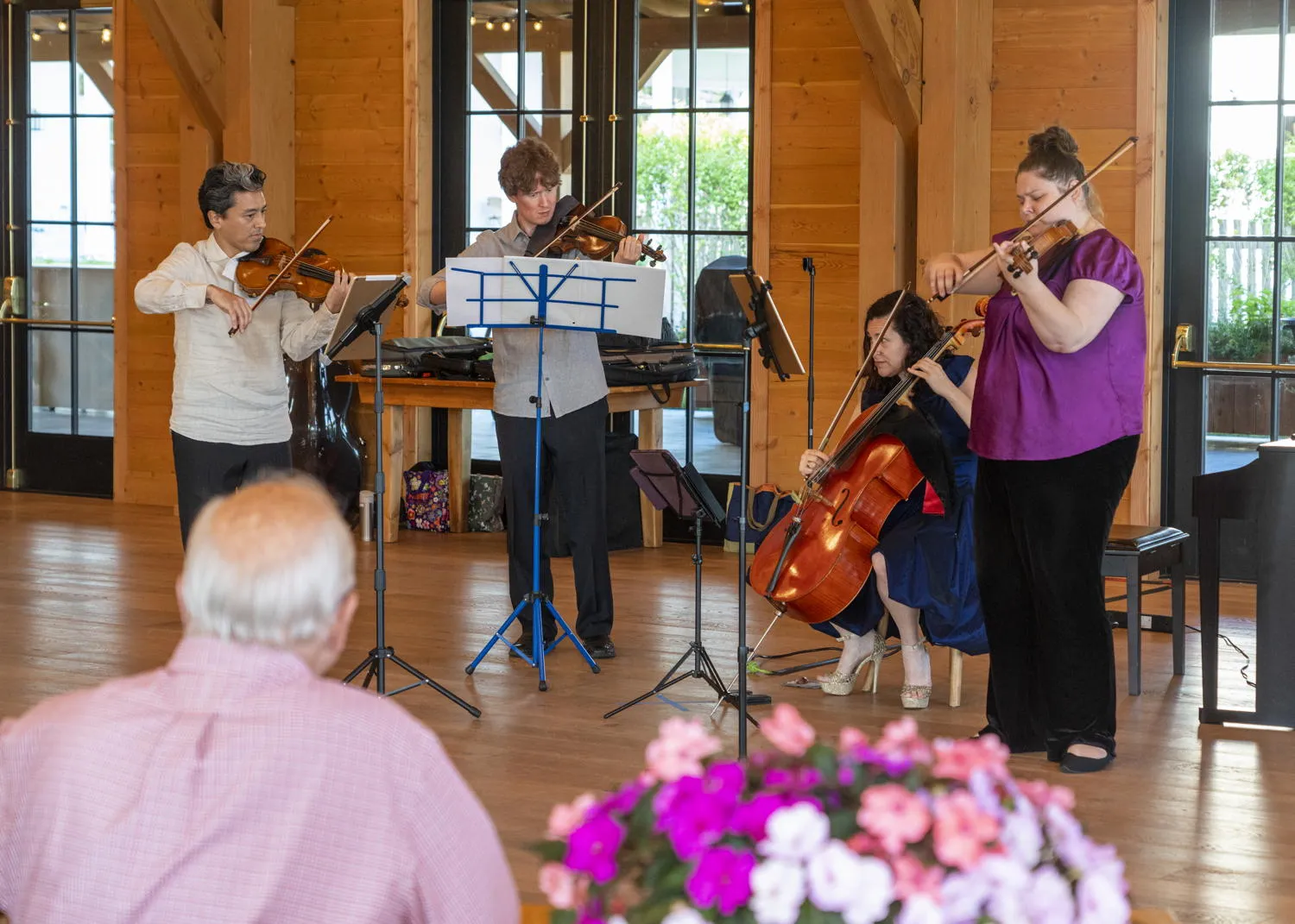 Four string players performing for diners in a wood-paneled hall