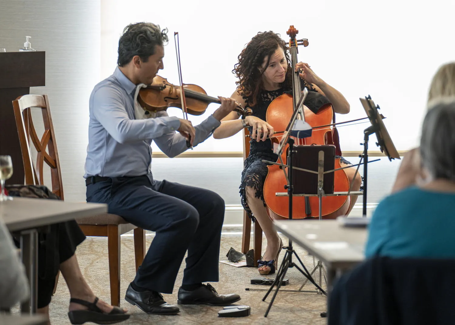 A violinist and a cellist performing for guests in a bright room