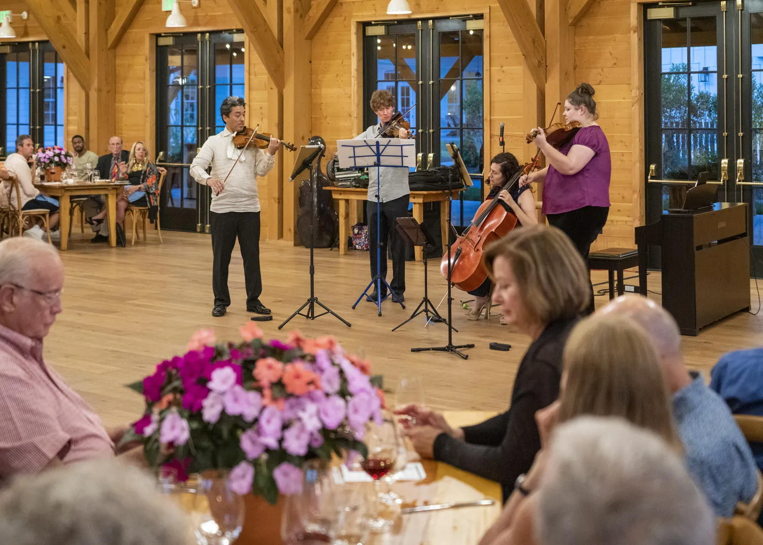 Diners watching four string players perform in the timber hall at the Lake House
