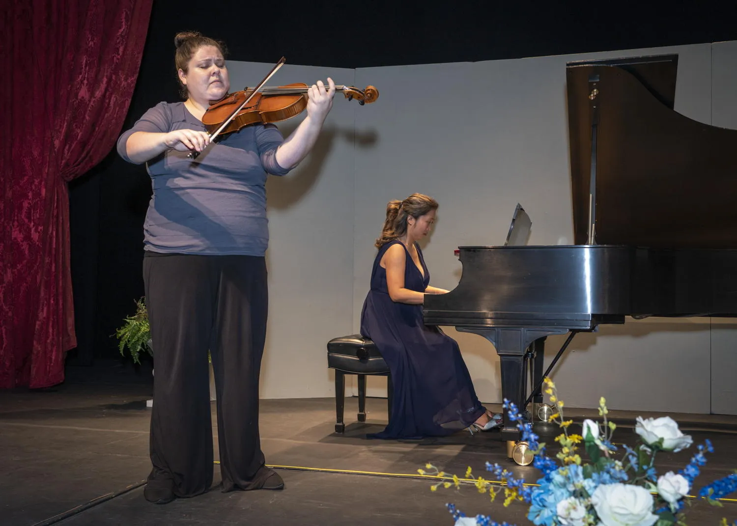 A string player standing beside a pianist at a grand piano on stage