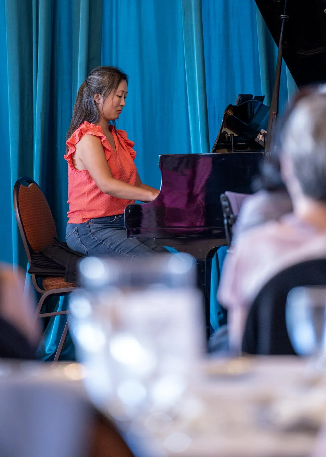 A pianist playing a grand piano in front of a teal curtain