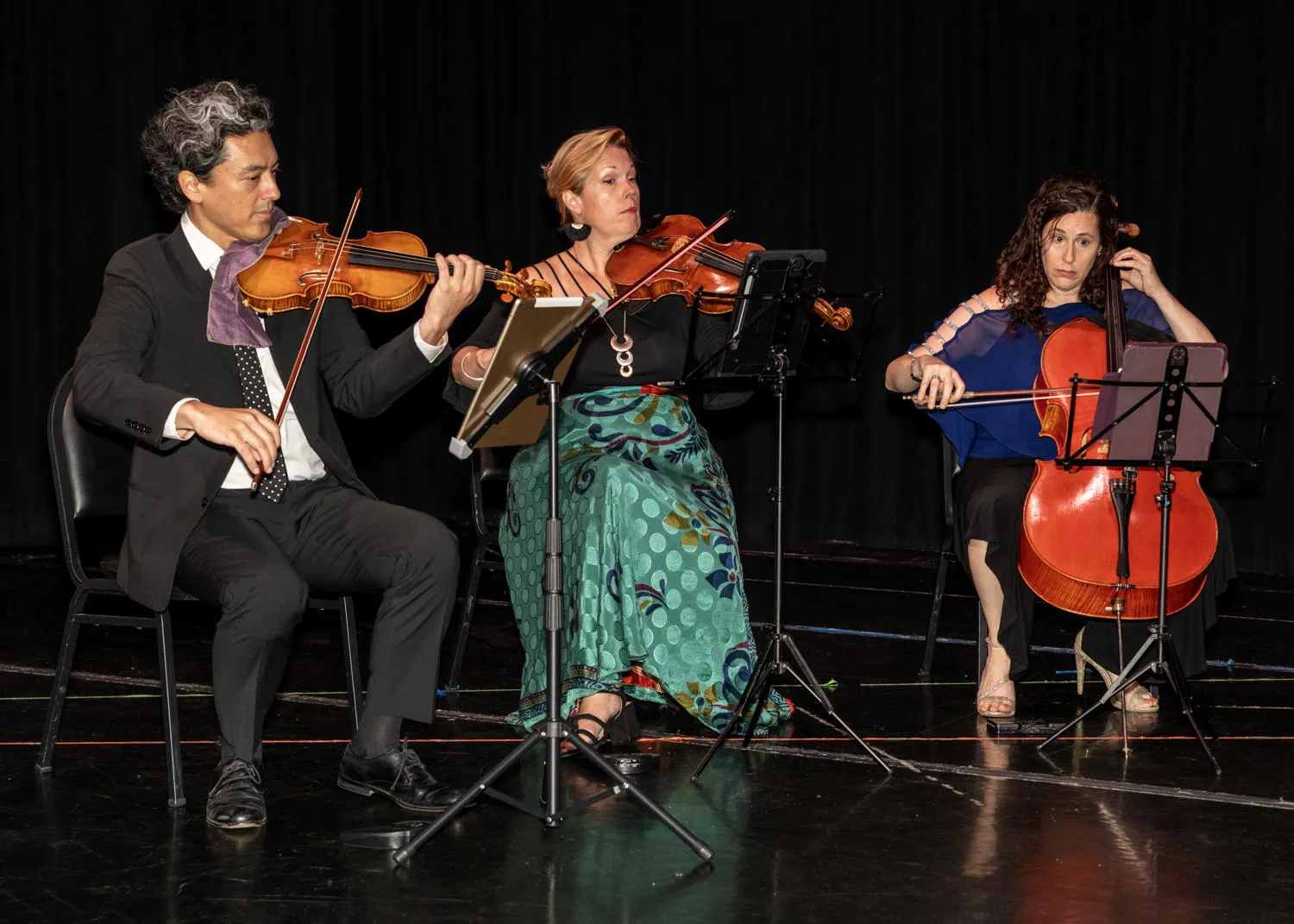 Three string players performing on a dark stage