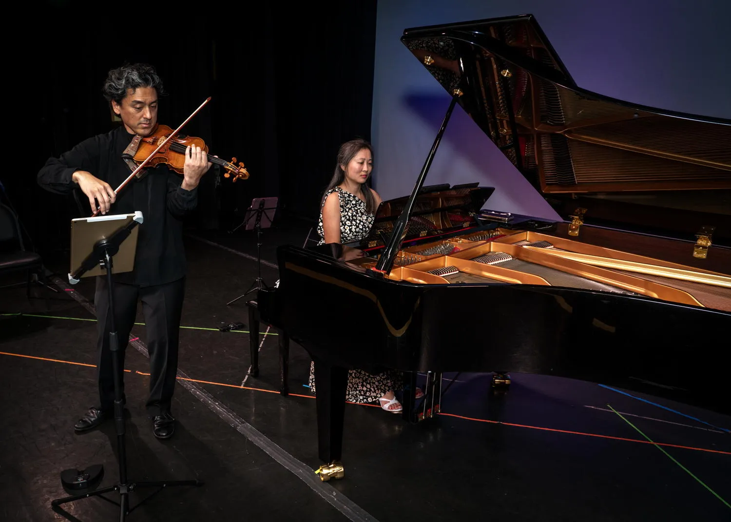 A violinist and a pianist performing beside an open grand piano