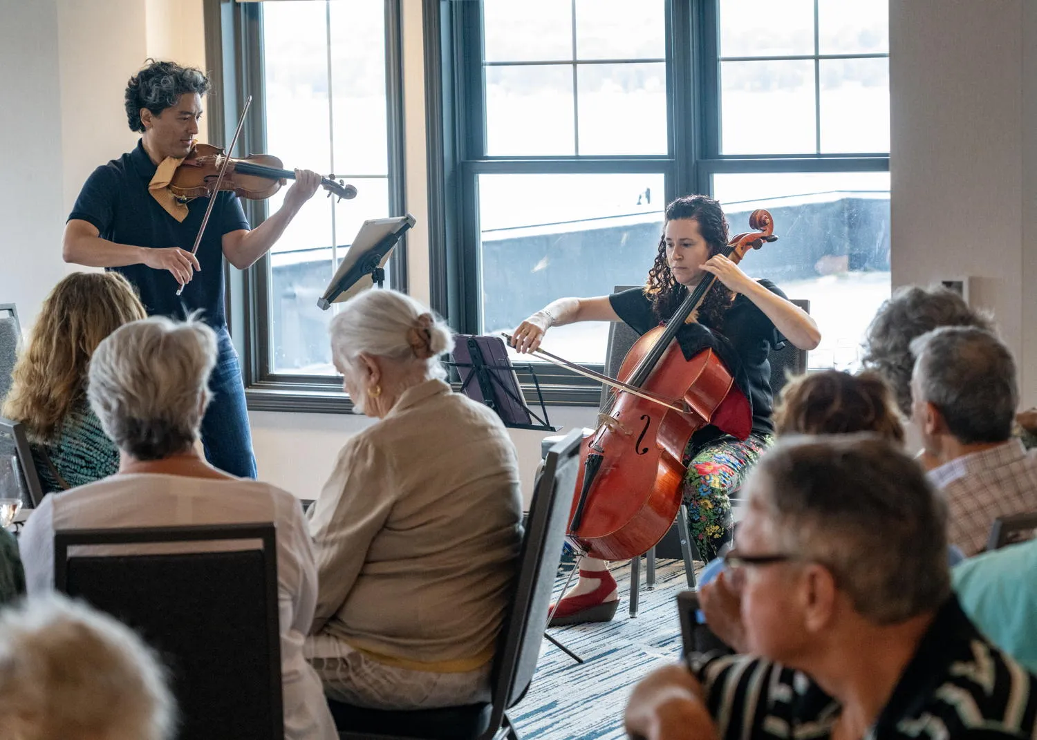 A violinist and a cellist performing by tall windows for seated guests
