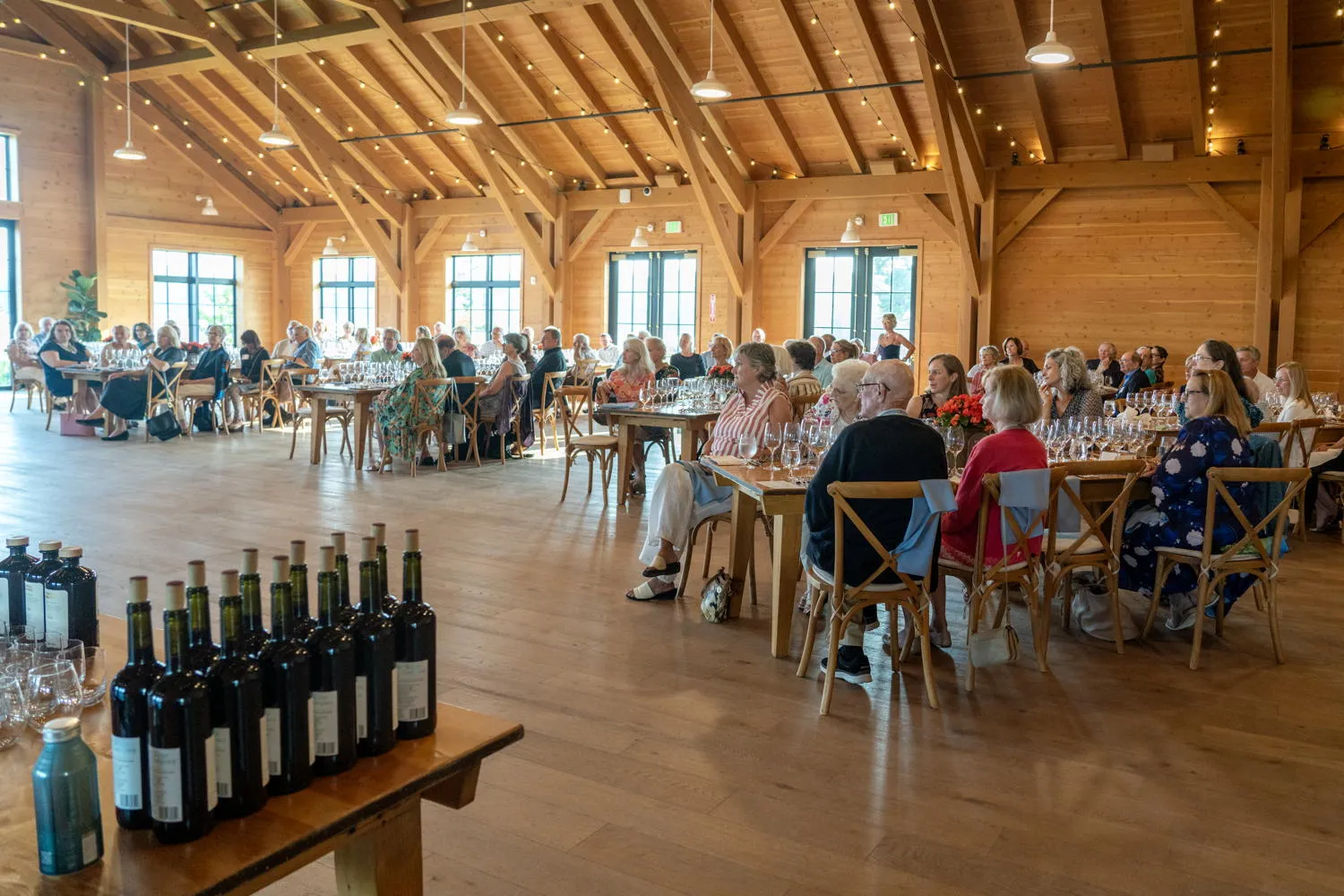 Guests seated at long tables in a timber-beamed hall, with wine bottles in the foreground