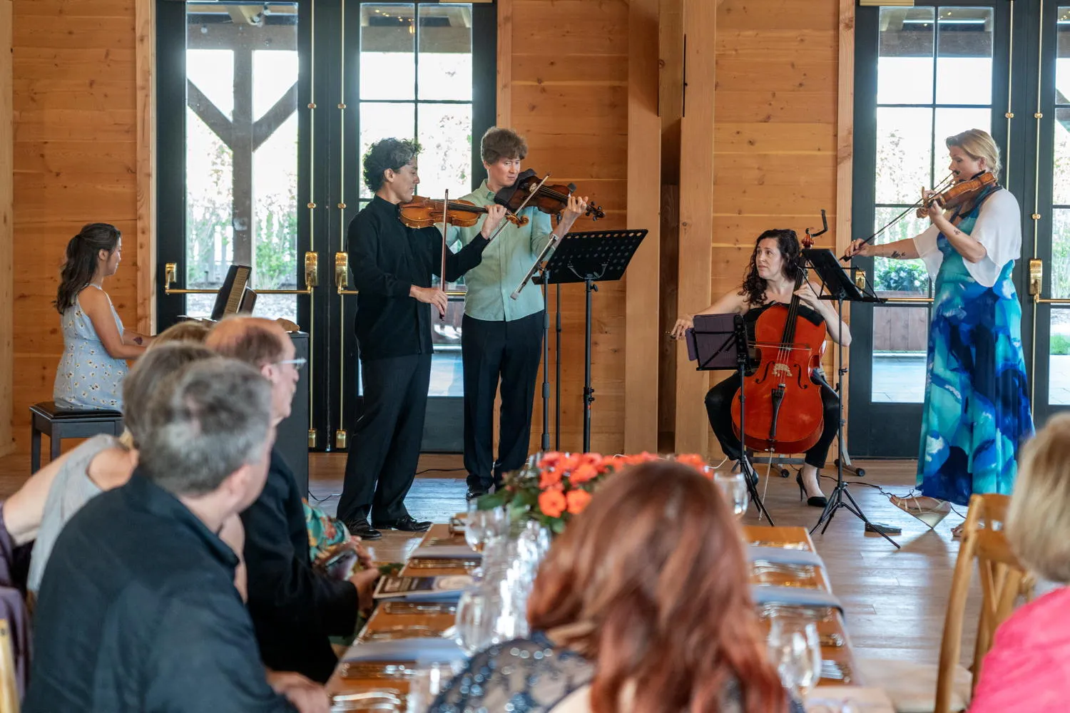 A pianist and four string players performing for diners in a wood-paneled hall