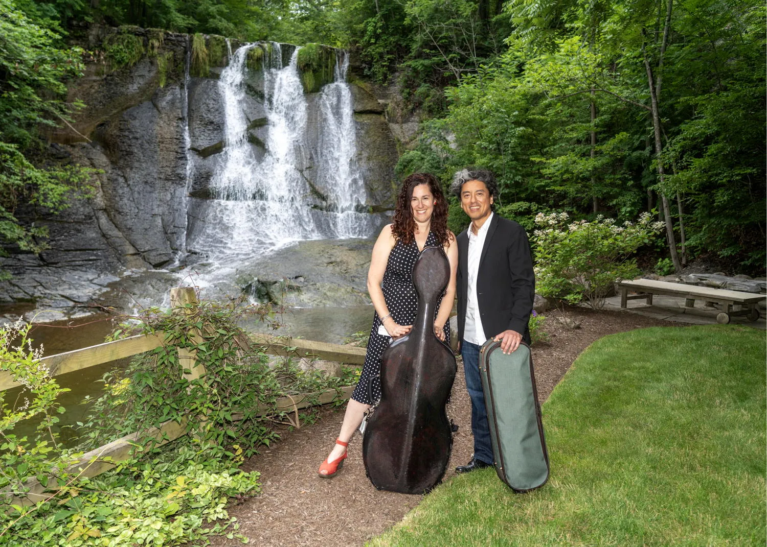 Two musicians with their instrument cases on a garden path beside a waterfall
