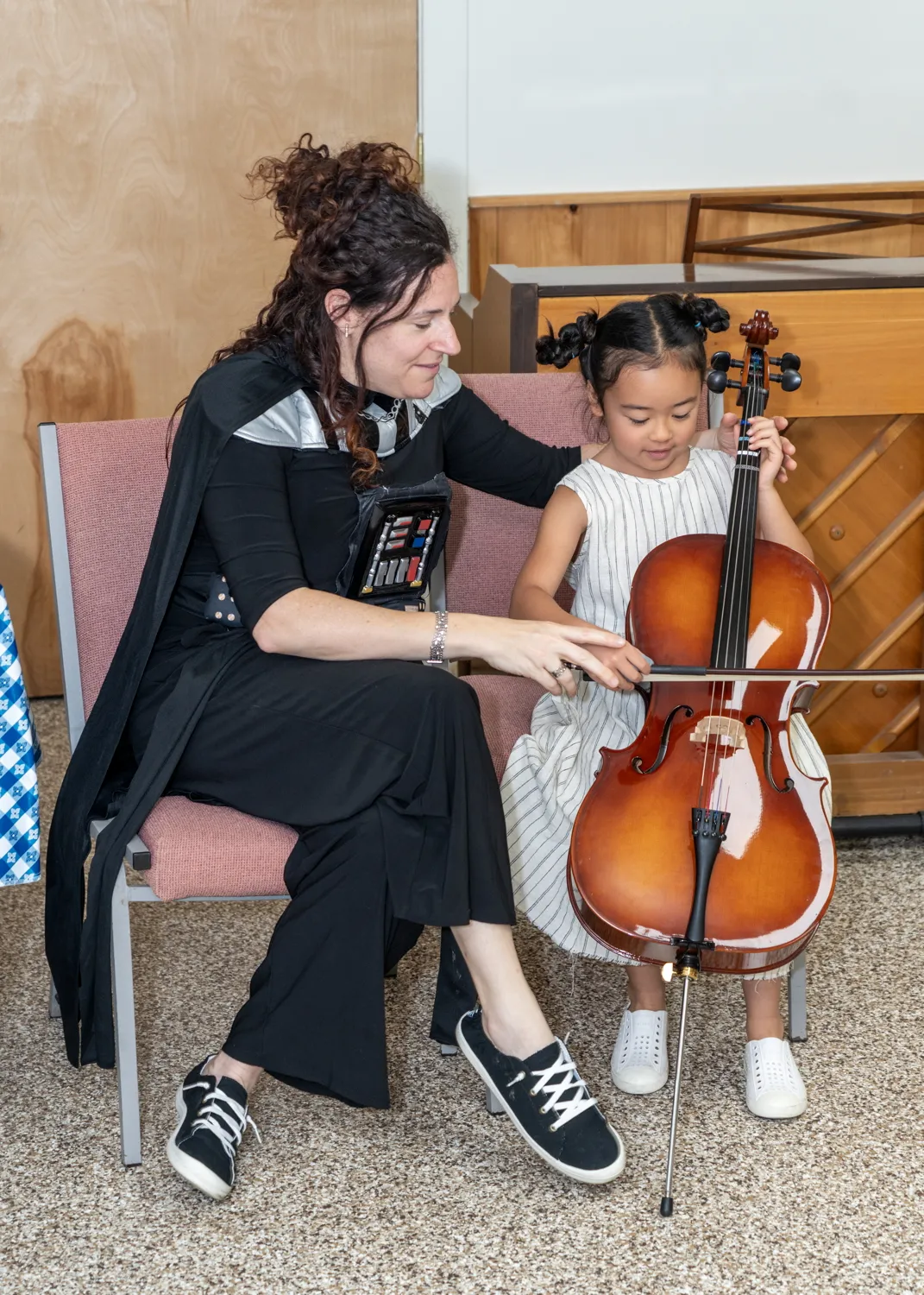 Amy Sue Barston, dressed as Darth Vader, helping a child bow a cello
