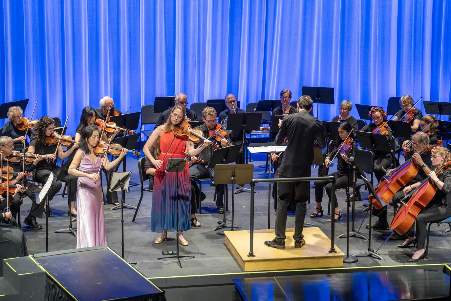Two soloists and the orchestra on stage under blue light