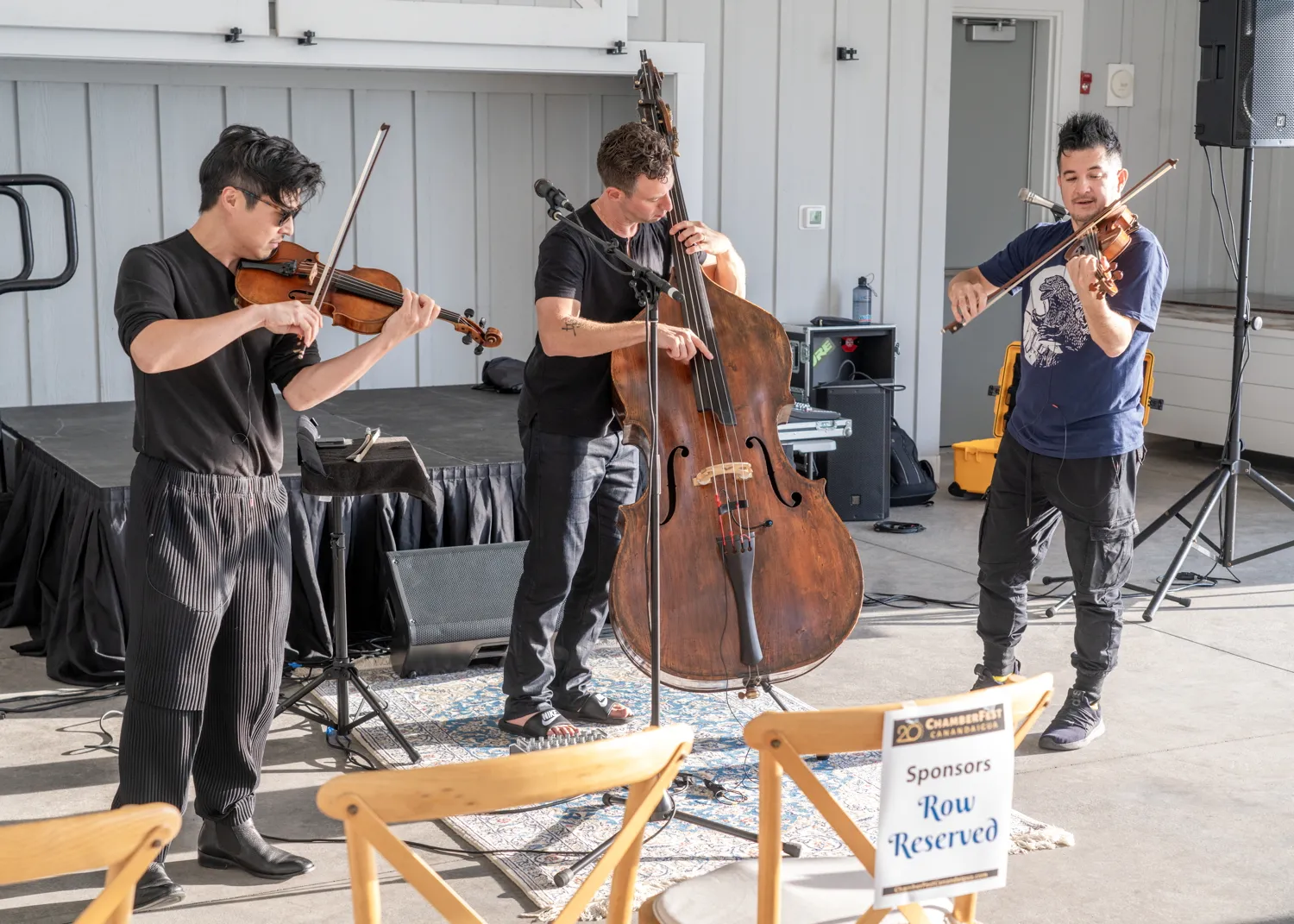 Two violinists and a double bassist playing together, with a Sponsors Row Reserved sign in front