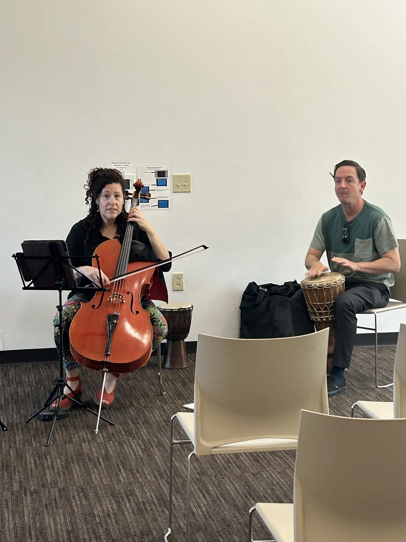 A cellist and a hand drummer playing in the library