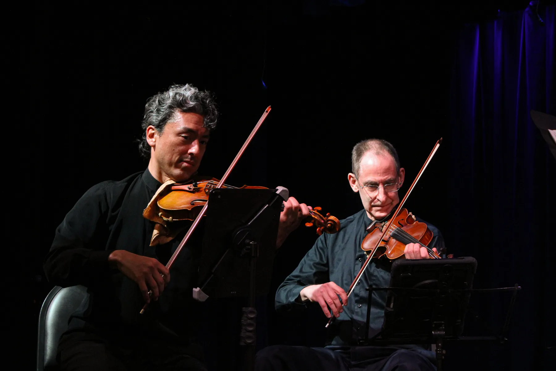 Two string players reading side by side under stage light