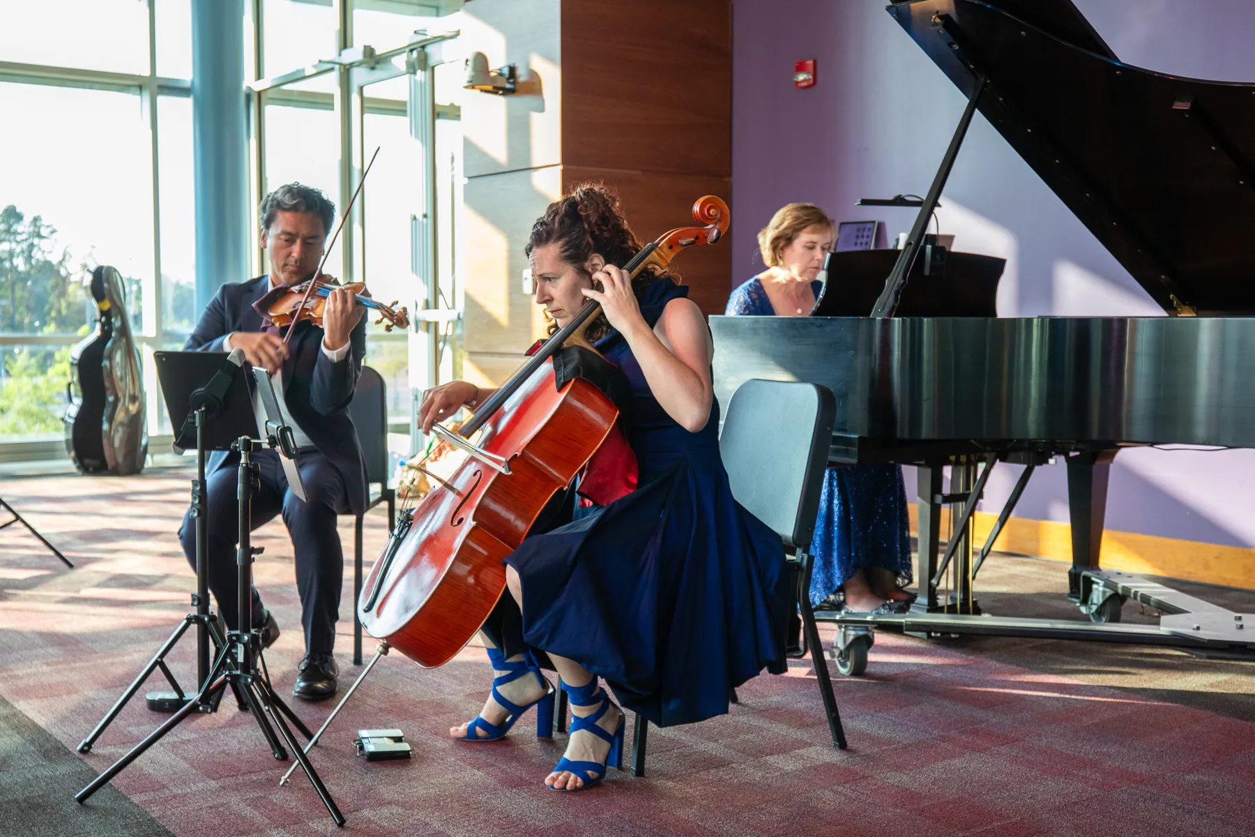 Violin, cello and piano playing beside tall windows