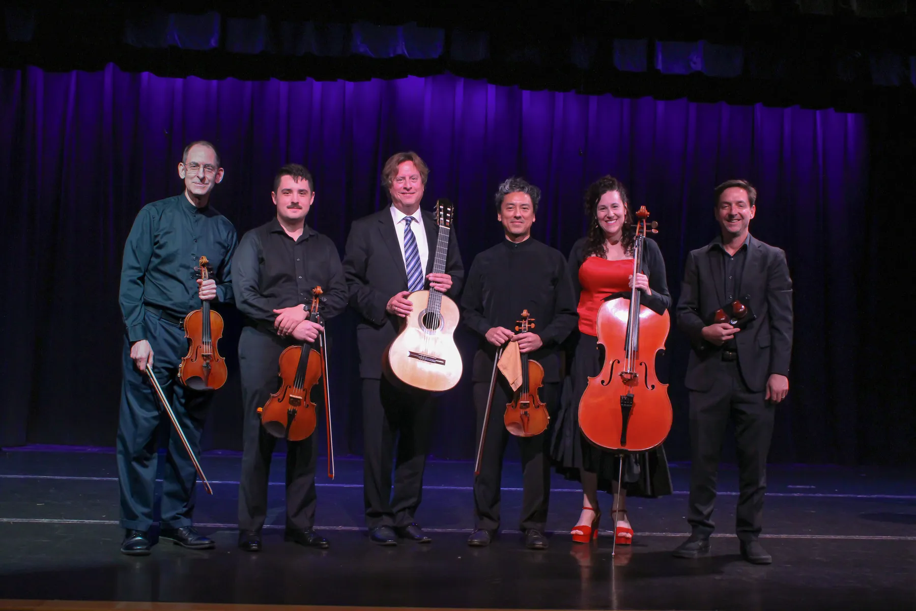 Six musicians standing on stage with their instruments
