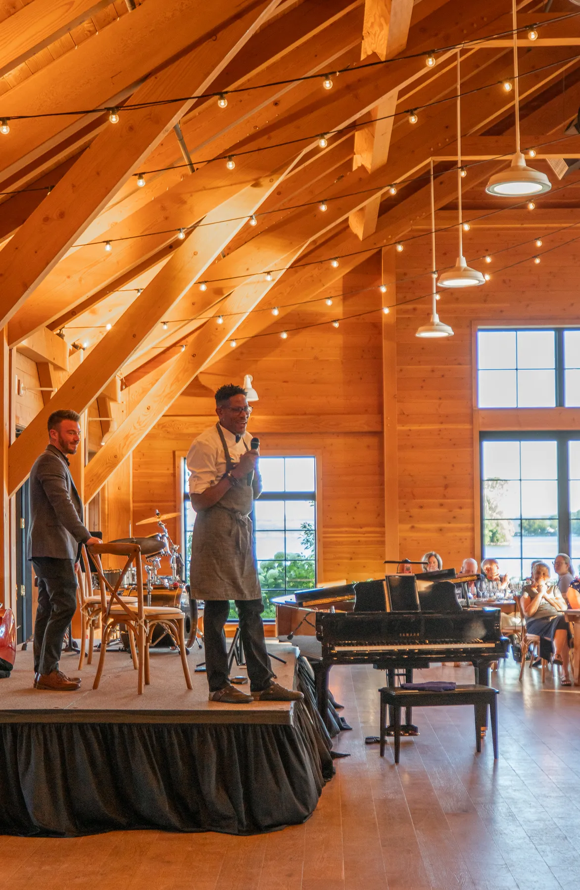 A chef in an apron speaking from the stage beside the piano