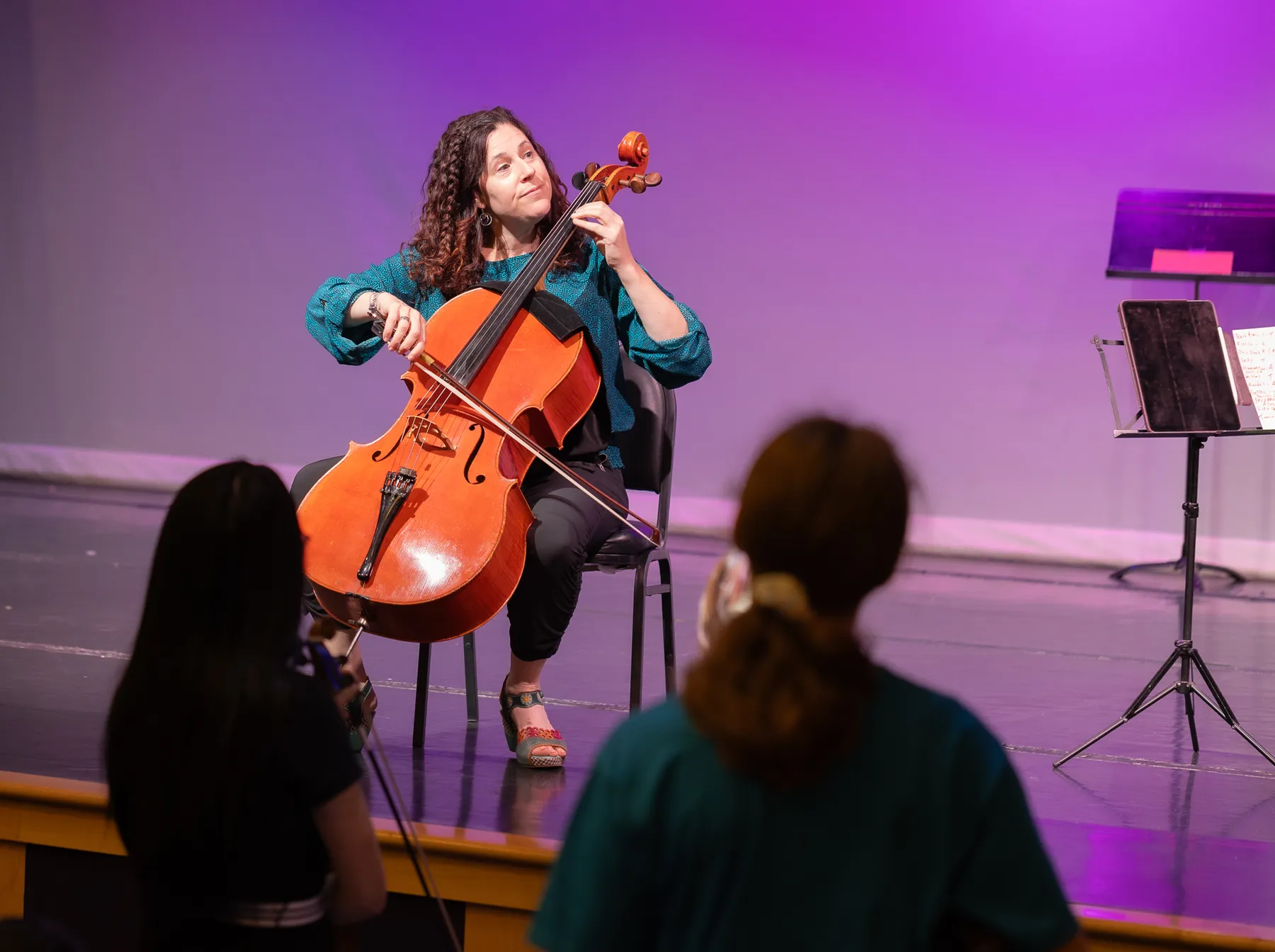 A cellist leading young players on stage
